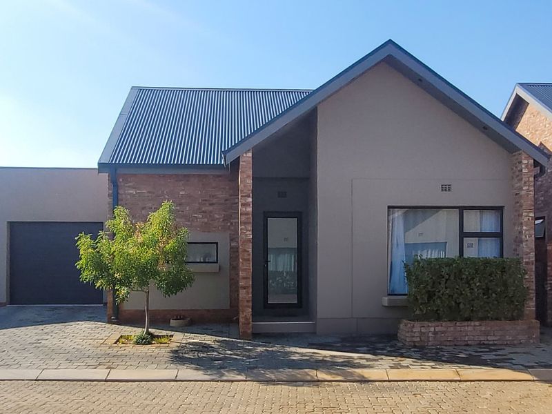 A modern townhouse exterior featuring a combination of brick and plaster finishes, a corrugated metal roof, and an integrated single garage.