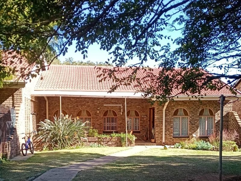 Front view of a face brick townhouse featuring a tiled roof, arched windows with security bars, and a well-maintained front garden with a paved walkway.