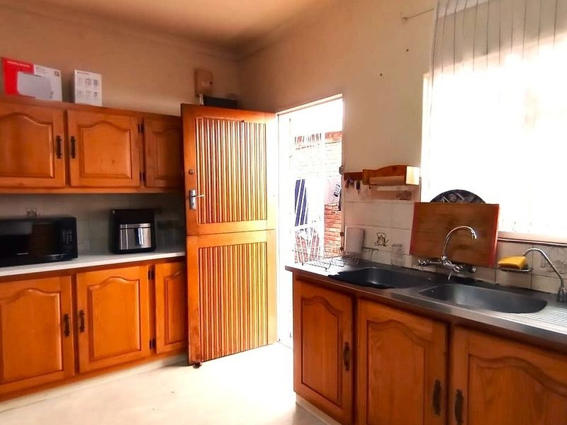 A dated kitchen featuring traditional wooden cabinetry, a double basin sink, and tiled splashbacks, offering potential for a modern renovation.