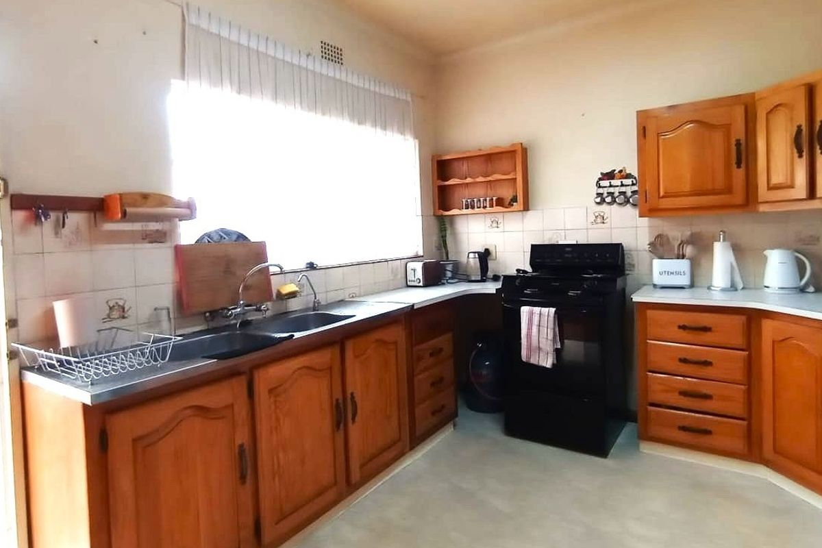 A dated kitchen featuring traditional wooden cabinetry, laminate countertops, a double sink, and a freestanding stove with tiled backsplash.
