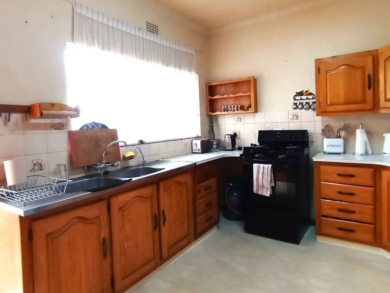 A dated kitchen featuring traditional wooden cabinetry, laminate countertops, a double sink, and a freestanding stove with tiled backsplash.