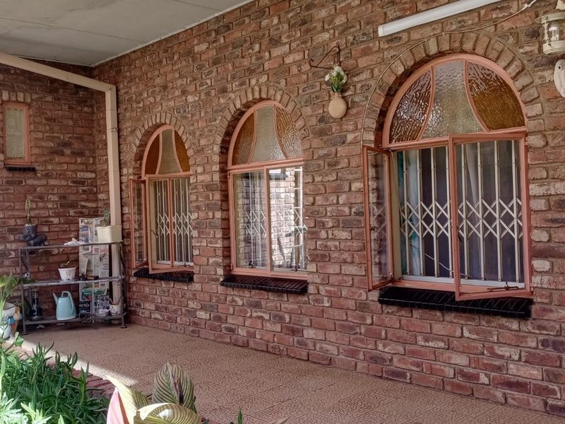 A covered patio area featuring exposed brick walls, arched windows with security gates, and tiled flooring, offering a classic outdoor living space.