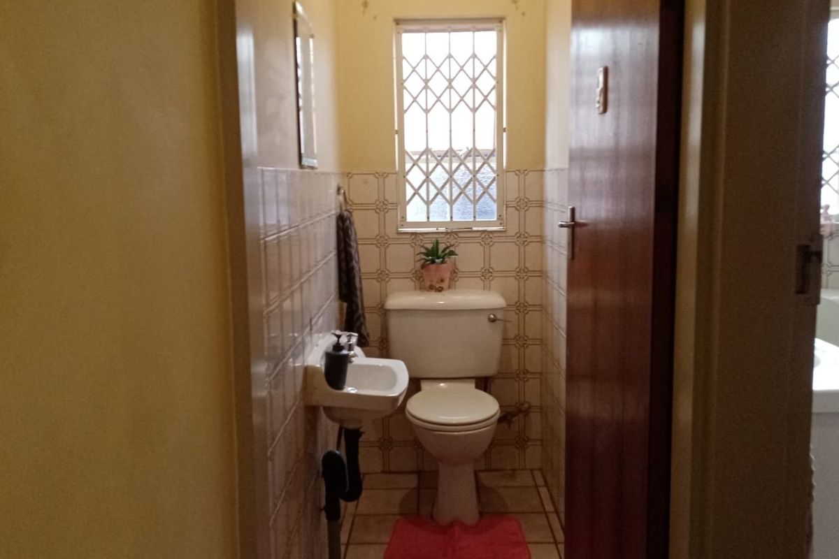 A compact guest bathroom featuring a wall-mounted basin, toilet, and tiled finishes, requiring modernization to improve its dated aesthetic.