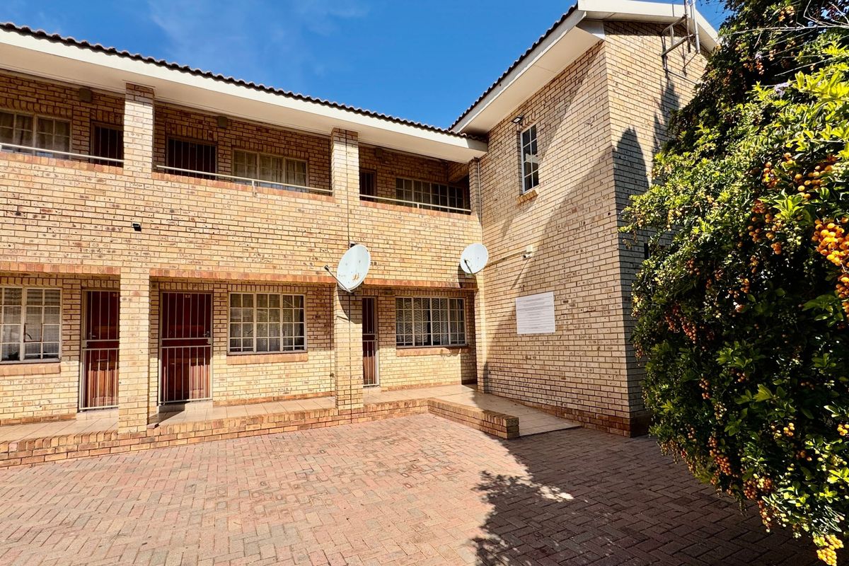 A view of the rear exterior of the apartment complex, featuring a paved courtyard, face brick facade, and balcony access.