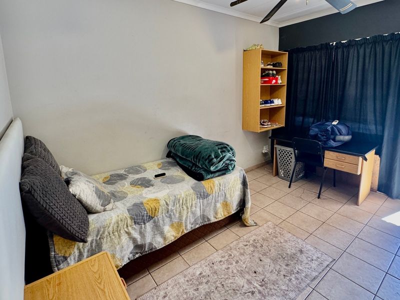 A functional bedroom featuring tiled flooring, a ceiling fan, and wall-mounted shelving, with direct access to an outdoor area.