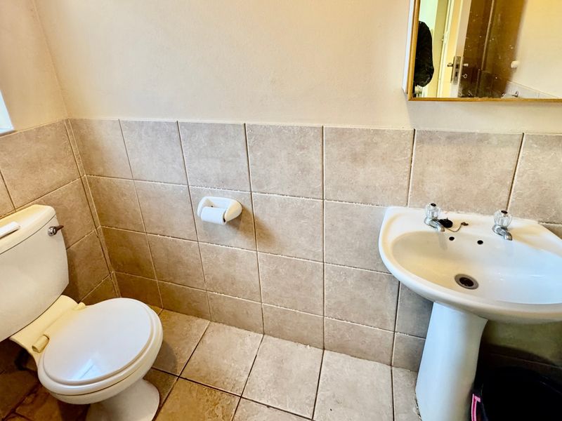A functional bathroom featuring a pedestal basin, dual flush toilet, and neutral ceramic tiling throughout.