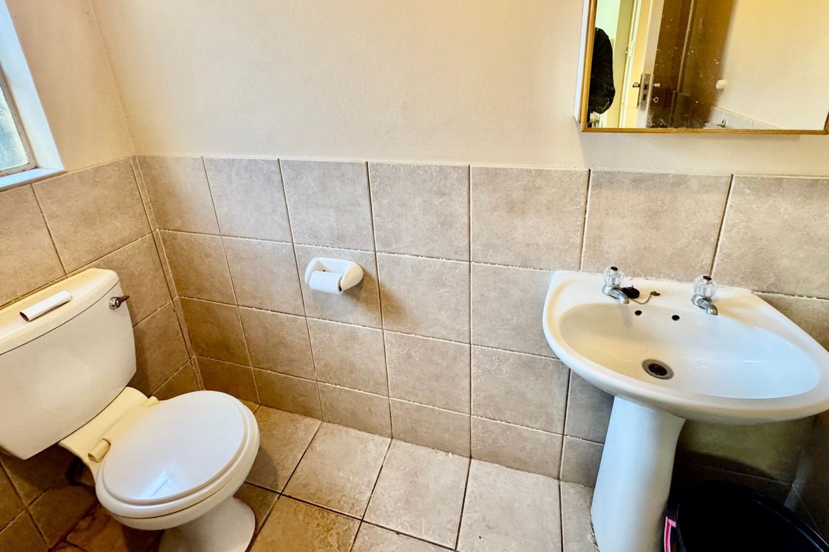 A functional bathroom featuring a pedestal basin, dual flush toilet, and neutral ceramic tiling throughout.