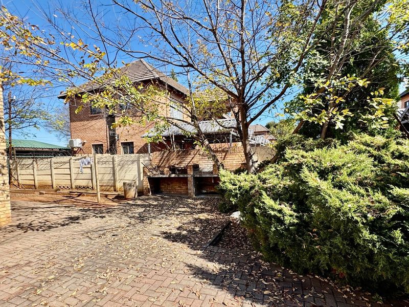 Rear exterior area featuring brick paving, a built-in braai, and perimeter walling with security fencing.