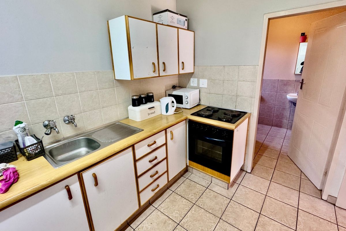 A functional kitchen featuring built-in cabinetry, a laminate countertop, stainless steel sink, and an integrated electric stove and oven with tiled backsplash.