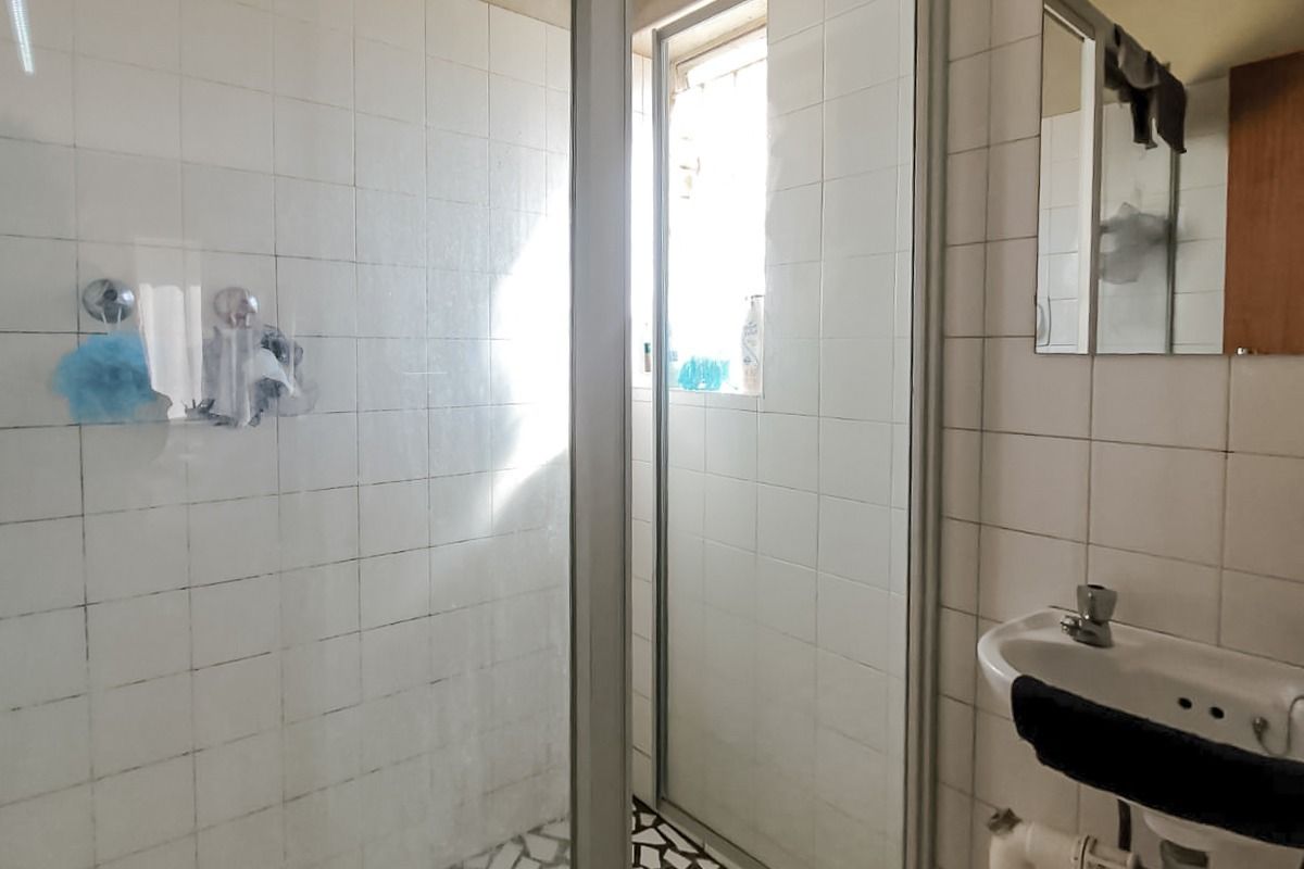 A functional bathroom featuring a shower enclosure with mosaic flooring, a wall-mounted basin, and tiled walls, requiring cosmetic updates to improve its overall condition.