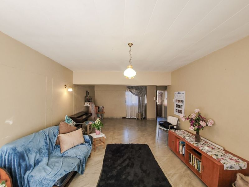 A spacious living area featuring neutral wall tones, tiled flooring, and classic pendant lighting, offering a versatile layout for comfortable daily living.