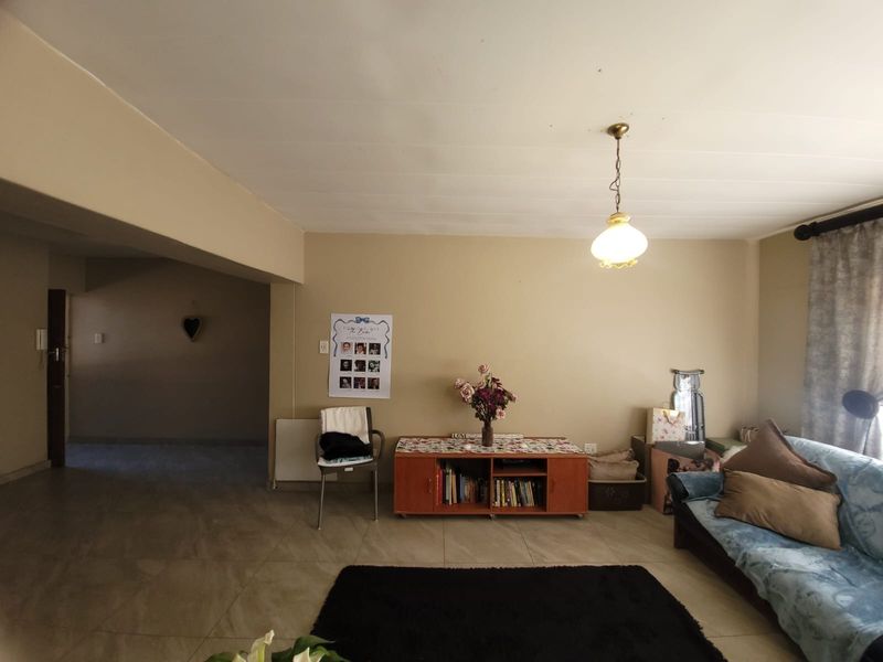 A living room area featuring neutral wall tones, tiled flooring, and a central pendant light fixture, offering a functional and open living space.