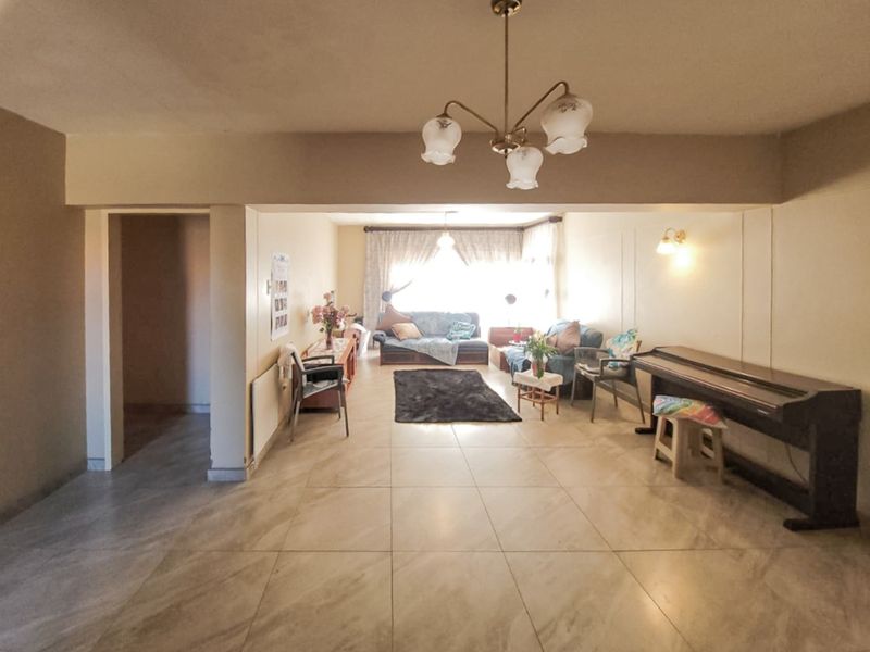 Spacious living area featuring neutral tiled flooring, a central ceiling light fixture, and an open-plan layout with an archway leading to adjacent spaces.