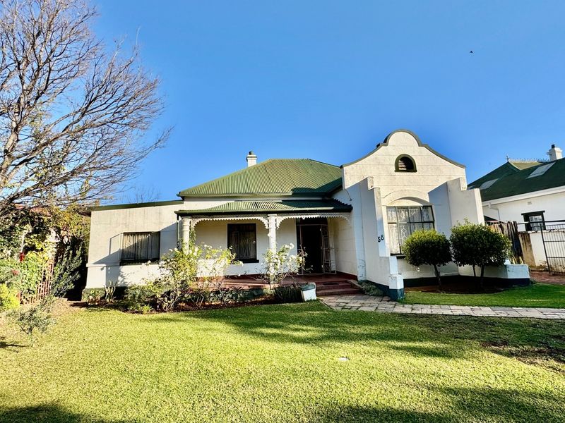 A charming front elevation of a house featuring a corrugated metal roof, a covered veranda with decorative fretwork, and a well-maintained front lawn.