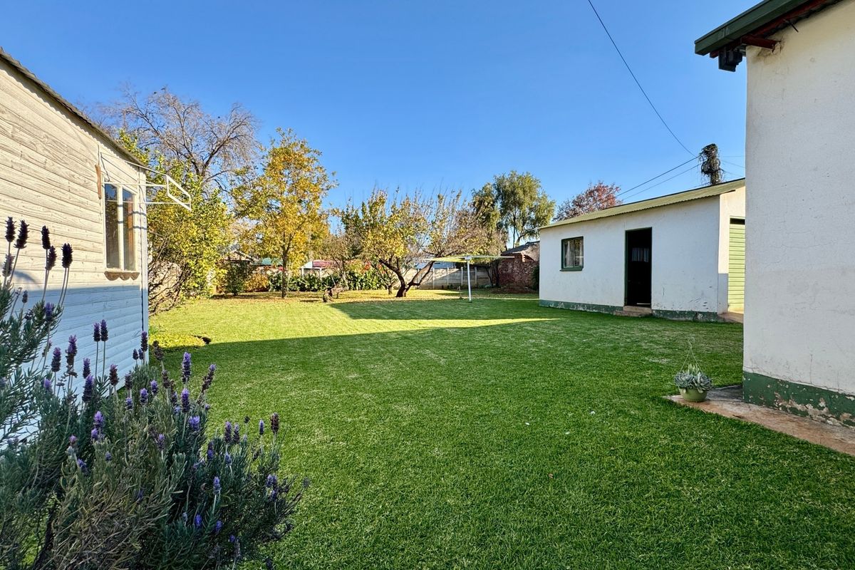 Spacious rear garden featuring a well-maintained lawn, established trees, and a detached outbuilding structure.
