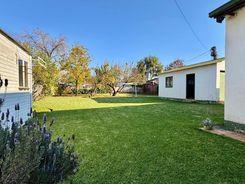 Spacious rear garden featuring a well-maintained lawn, established trees, and a detached outbuilding structure.