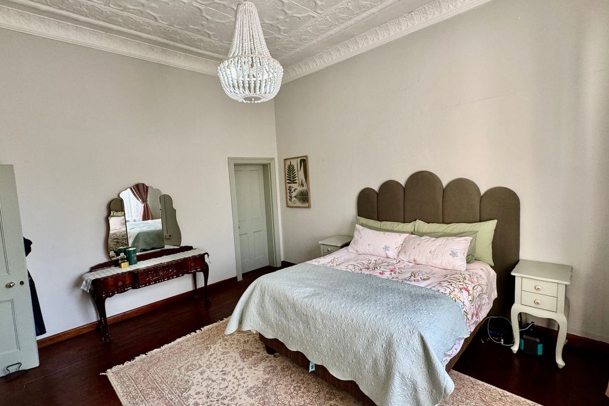 Spacious bedroom featuring high ceilings with ornate decorative cornicing, a classic ceiling rose, and polished hardwood flooring.