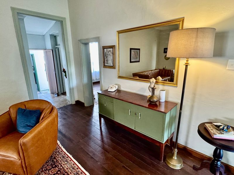 A living area featuring original hardwood flooring and classic architectural detailing, providing a warm and character-filled space with access to adjacent rooms.