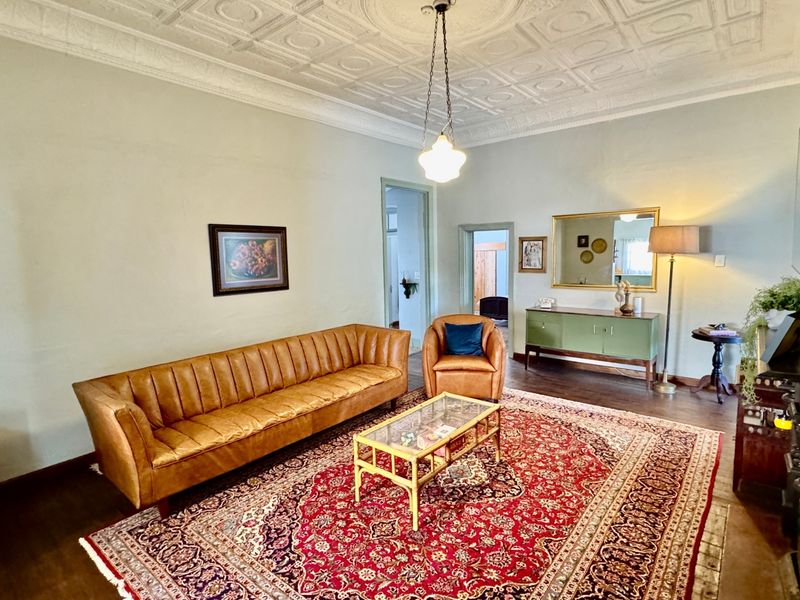 Spacious living room featuring a classic pressed metal ceiling, ornate ceiling rose, and original hardwood flooring, offering a character-filled space with period charm.