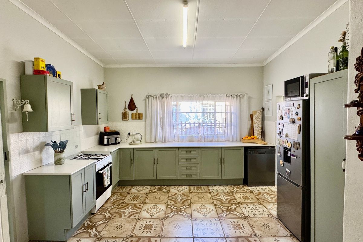 A functional kitchen featuring sage green cabinetry, patterned floor tiles, a gas hob, and ample counter space with a window overlooking the exterior.