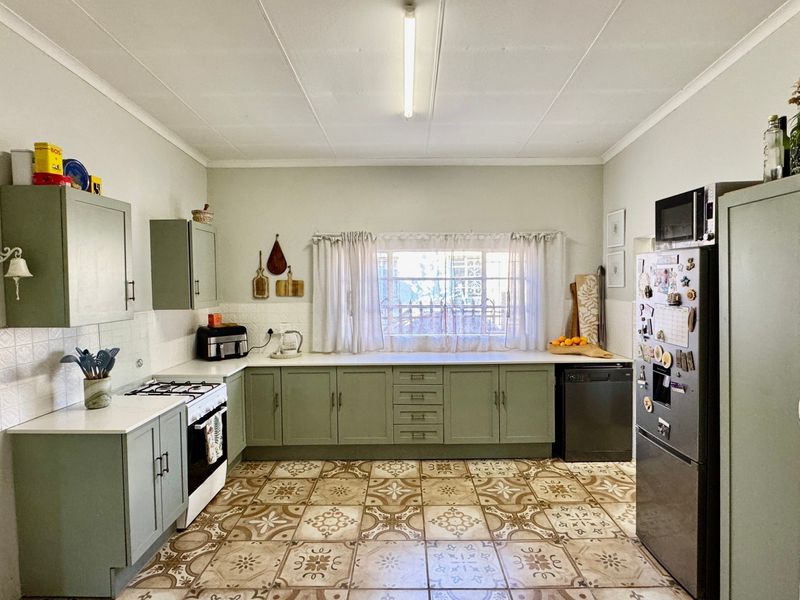 A functional kitchen featuring sage green cabinetry, patterned floor tiles, a gas hob, and ample counter space with a window overlooking the exterior.