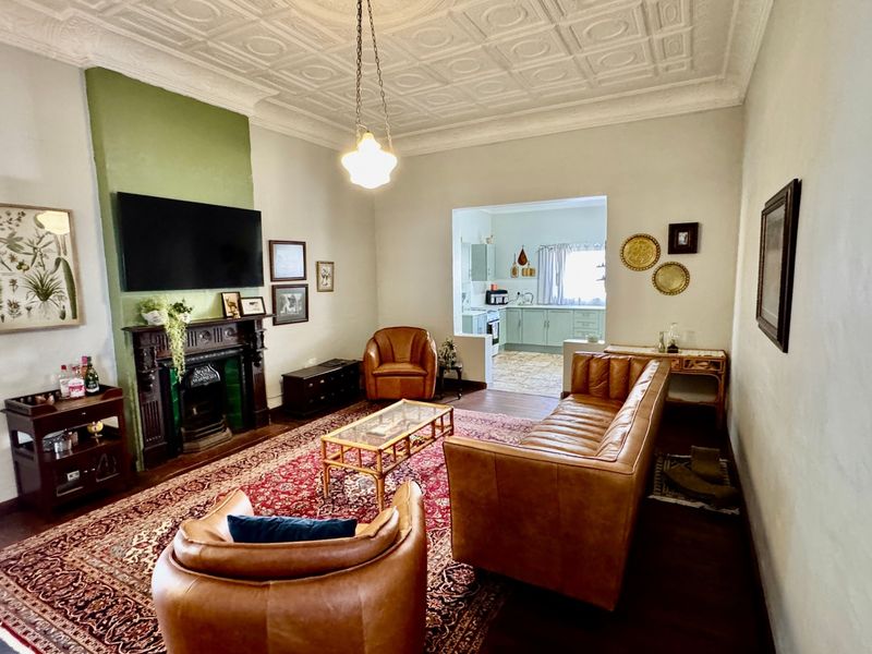 Spacious living room featuring a classic period fireplace, ornate pressed metal ceilings, and polished timber flooring, with an open transition to the kitchen area.