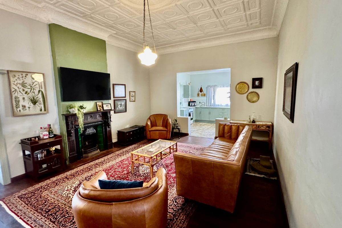 Spacious living room featuring a classic period fireplace, ornate pressed metal ceilings, and polished timber flooring, with an open transition to the kitchen area.