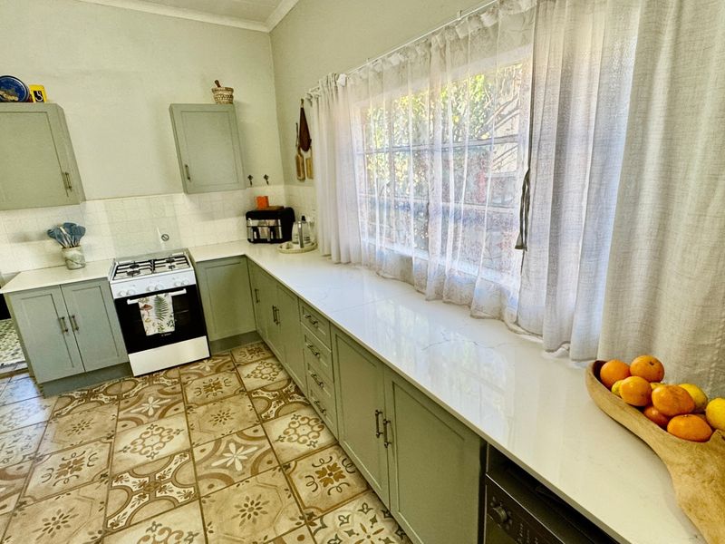 A well-maintained kitchen featuring sage green cabinetry, white quartz countertops, a gas stove, and decorative patterned floor tiles.