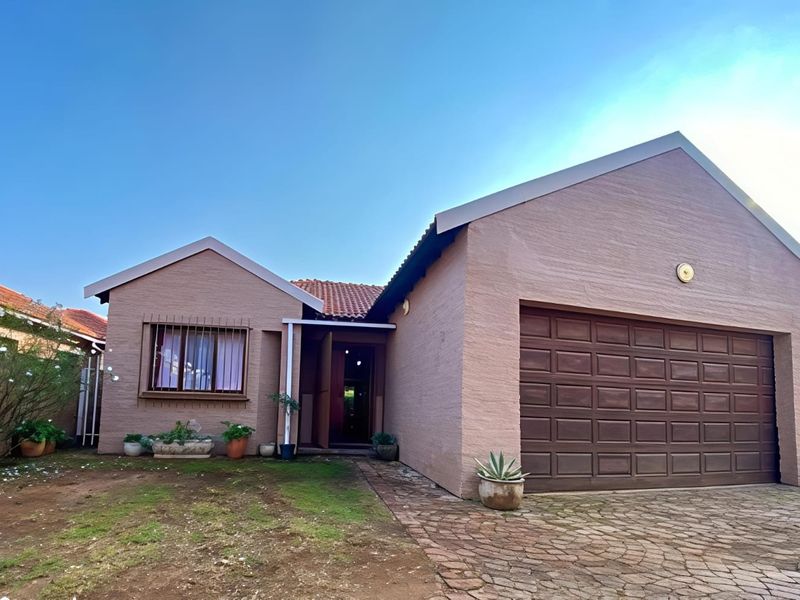 Front elevation of a townhouse featuring a double garage, paved driveway, and a tiled roof with security bars on the windows.