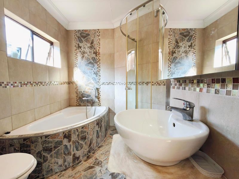 A dated bathroom featuring a corner bathtub, glass shower enclosure, and a vessel sink with mosaic tile accents throughout the space.