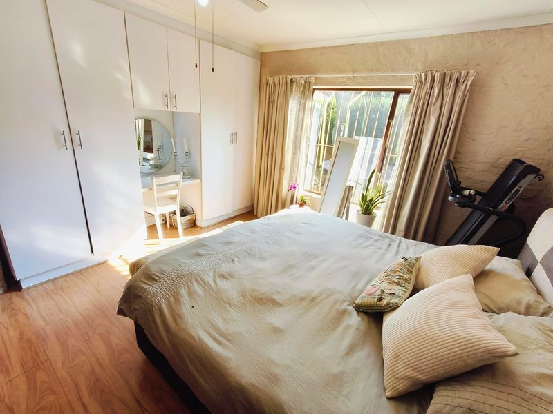 A well-lit bedroom featuring laminate flooring, extensive built-in cupboards with a vanity nook, and security bars on the window.