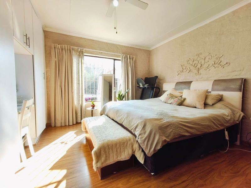 A spacious bedroom featuring laminate flooring, built-in cupboards, and a ceiling fan, with natural light entering through a large window.