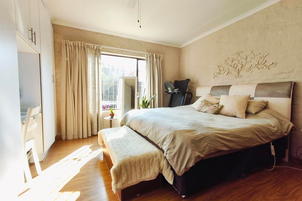 A spacious bedroom featuring laminate flooring, built-in cupboards, and a ceiling fan, with natural light entering through a large window.
