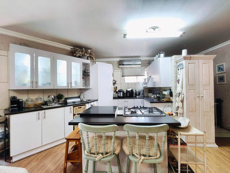 A functional kitchen featuring white cabinetry, a central island with a gas hob, dark countertops, and laminate flooring.