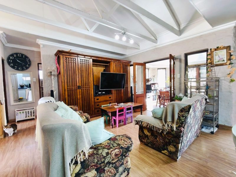 Spacious living room featuring exposed timber ceiling trusses, laminate flooring, and built-in wooden cabinetry, with french doors leading to an adjacent dining area.