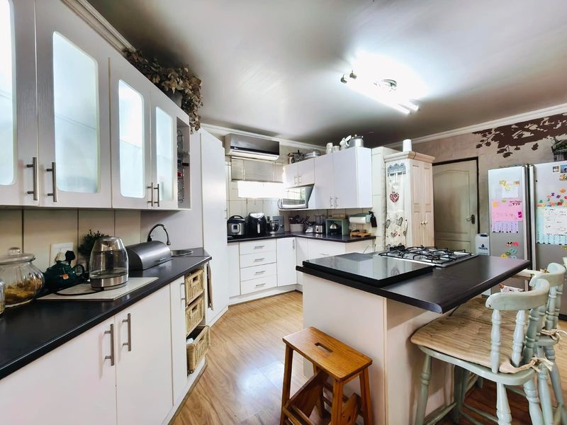 A functional kitchen featuring white cabinetry, dark laminate countertops, a gas hob, and an integrated air conditioning unit.
