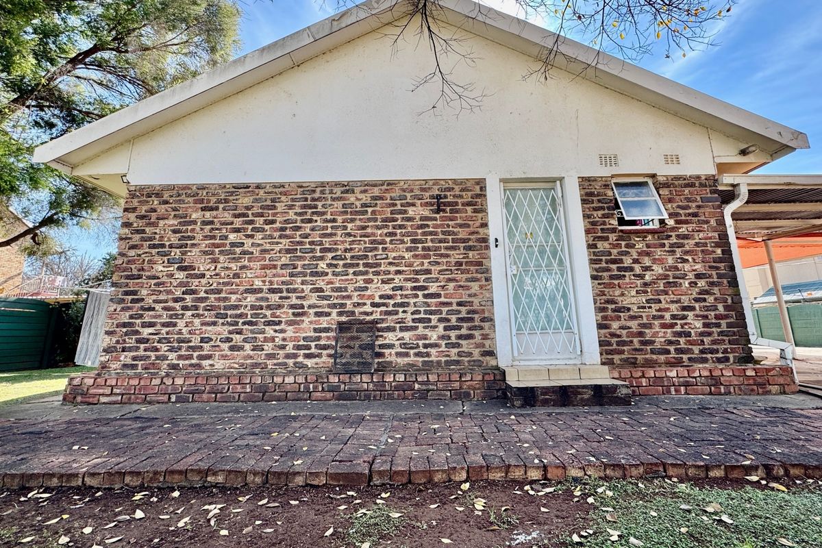 Rear exterior view of the house featuring a face brick facade, paved patio area, and a secure entrance door.