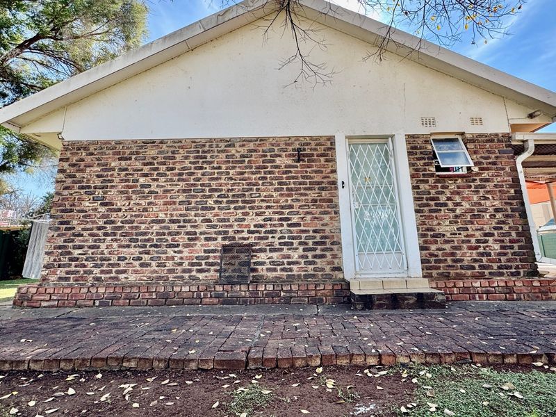 Rear exterior view of the house featuring a face brick facade, paved patio area, and a secure entrance door.