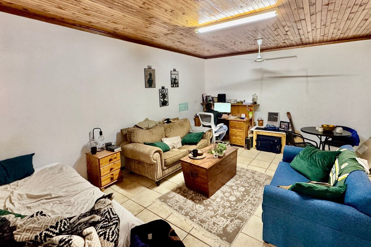 A living room featuring ceramic floor tiles and a timber tongue and groove ceiling with an integrated ceiling fan.