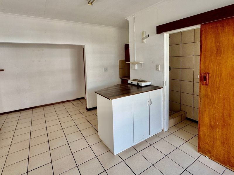 An open-plan living area featuring tiled flooring, a compact kitchenette unit, and a sliding door leading to a tiled shower enclosure.