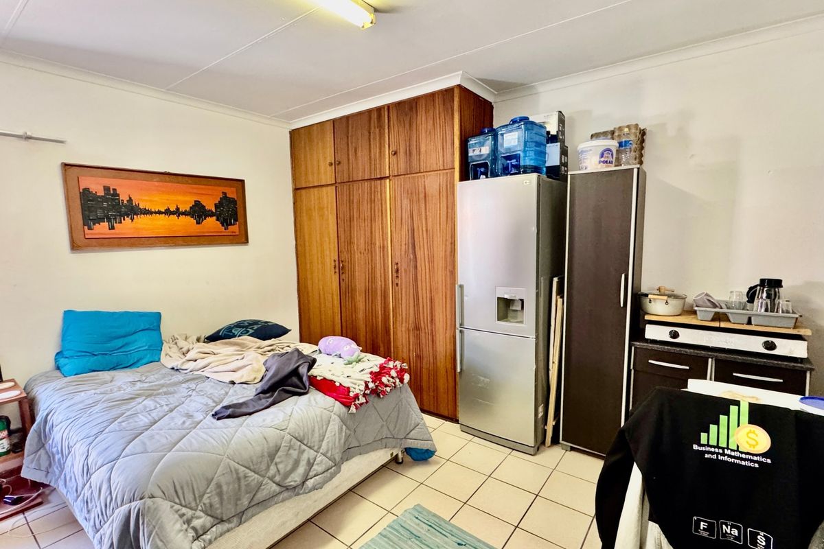 A bedroom featuring built-in wooden cupboards, tiled flooring, and a coved ceiling, offering a functional space with potential for modernization.