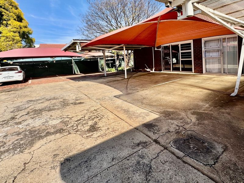 Spacious paved driveway area featuring multiple shade sail structures, providing ample covered parking space in front of the main building entrance.
