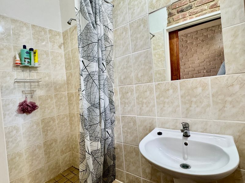 A functional bathroom featuring a pedestal basin, shower area with curtain, and tiled finishes, currently requiring cosmetic updates to the wall surfaces.