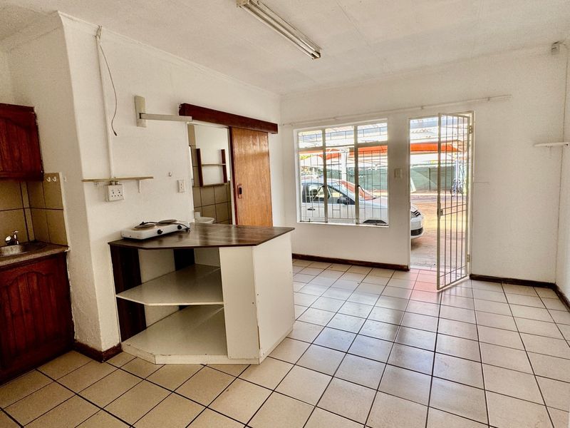 Open plan kitchen and living area featuring tiled flooring, built-in wooden cabinetry, and direct access to the exterior via a security gate.