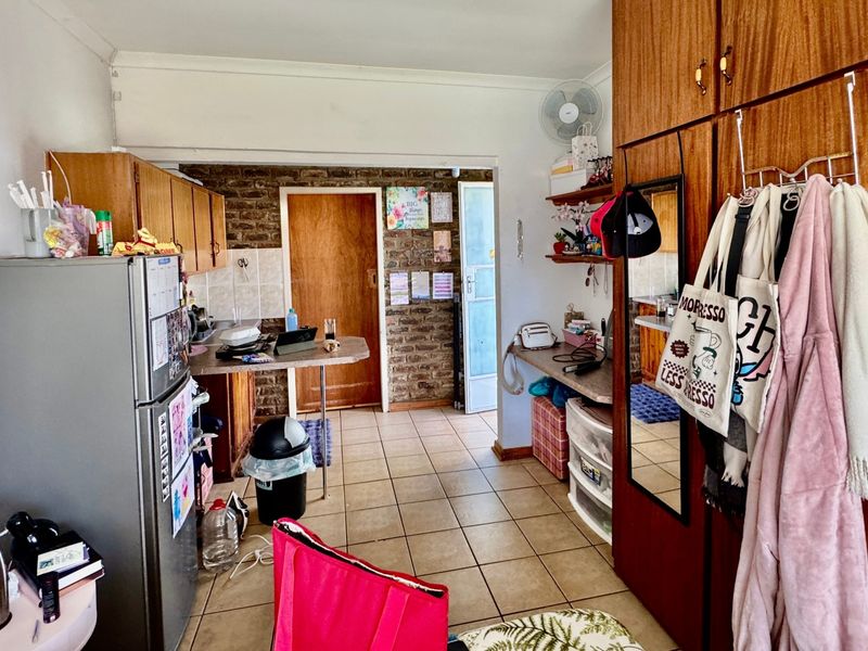 A functional kitchen area featuring tiled flooring, built-in wooden cabinetry, and an exposed brick feature wall, offering potential for modernization and layout optimization.