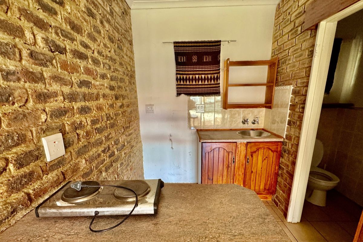 A compact kitchen area featuring exposed brick walls, wooden cabinetry, a built-in sink, and tiled splashback, offering a rustic aesthetic.