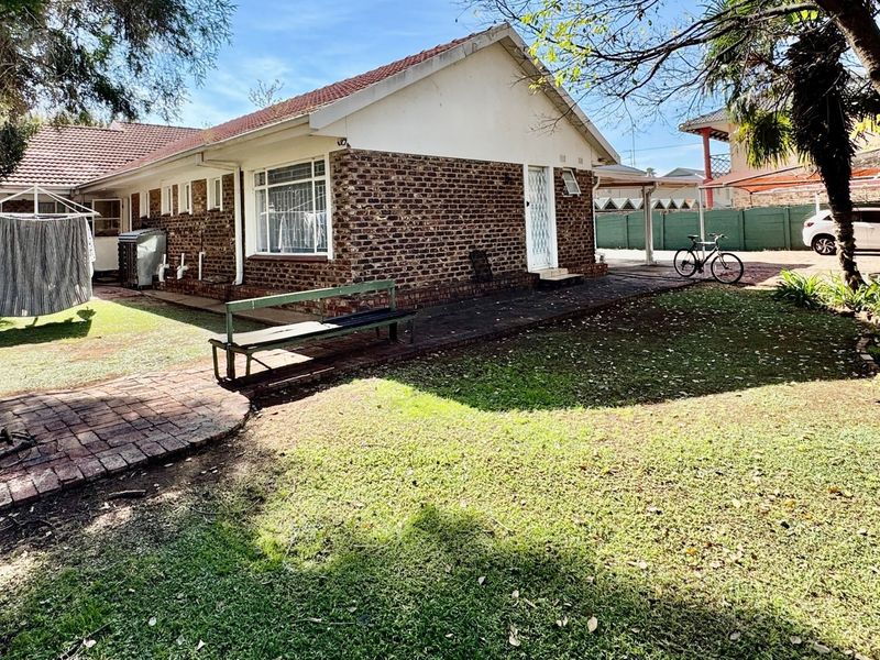 Rear view of the property featuring a brick facade, tiled roof, and paved walkway leading through the garden area.
