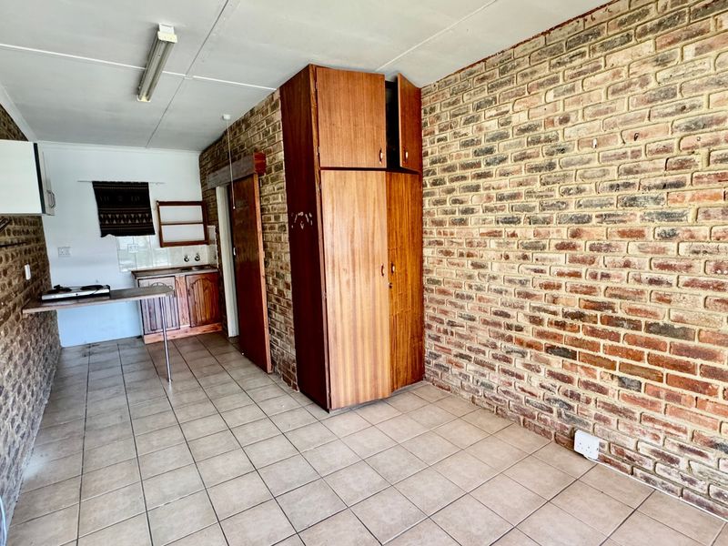 Open plan living area featuring exposed brick walls, tiled flooring, and a compact kitchenette with built-in cabinetry and storage.