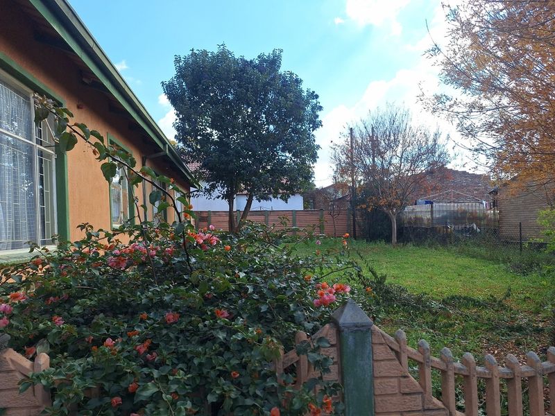 A view of the rear garden area featuring a lawn, established trees, and a precast concrete boundary wall.