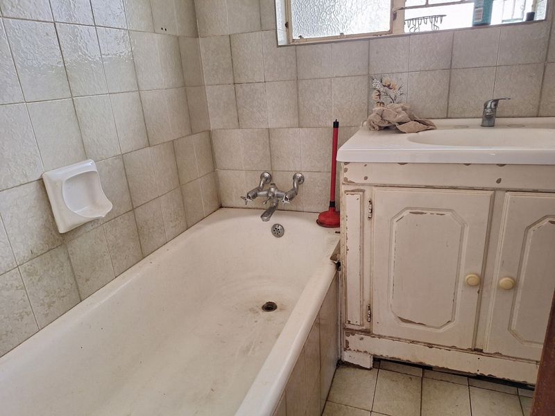 A dated bathroom featuring a standard bathtub, basin, and vanity cabinet with visible wear on the cabinetry and wall tiles.